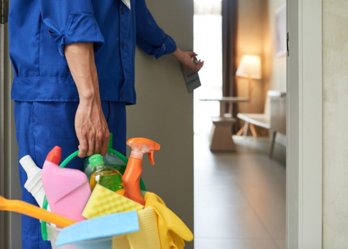 Professional cleaner with bucket of detergents opening room