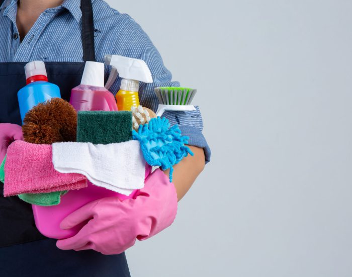 Young girl is holding cleaning product, gloves and rags in the basin on white background